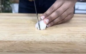 Person chopping onion on a wooden cutting board in a kitchen, close-up detail.